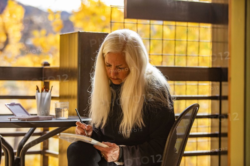 Woman with long white hair painting watercolors on deck in autumn, Springdale, Utah, USA