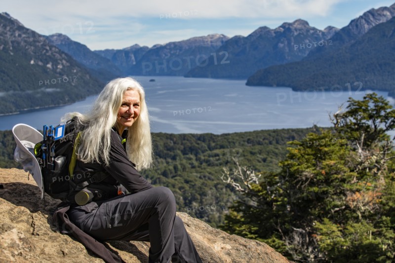 Portrait of smiling female hiker with long white hair sitting on rock above mountain lakes, Bariloche, , Argentina