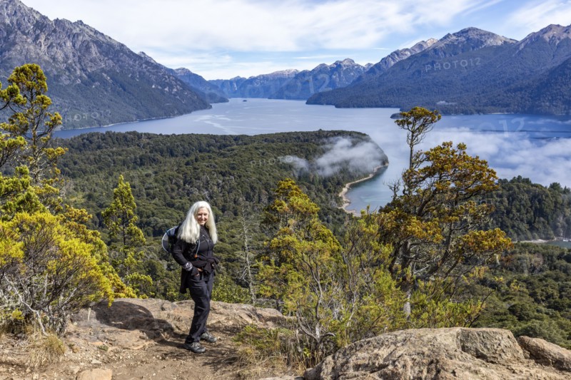 Smiling woman with long white hair standing on top of hill above mountain lakes, Bariloche, , Argentina
