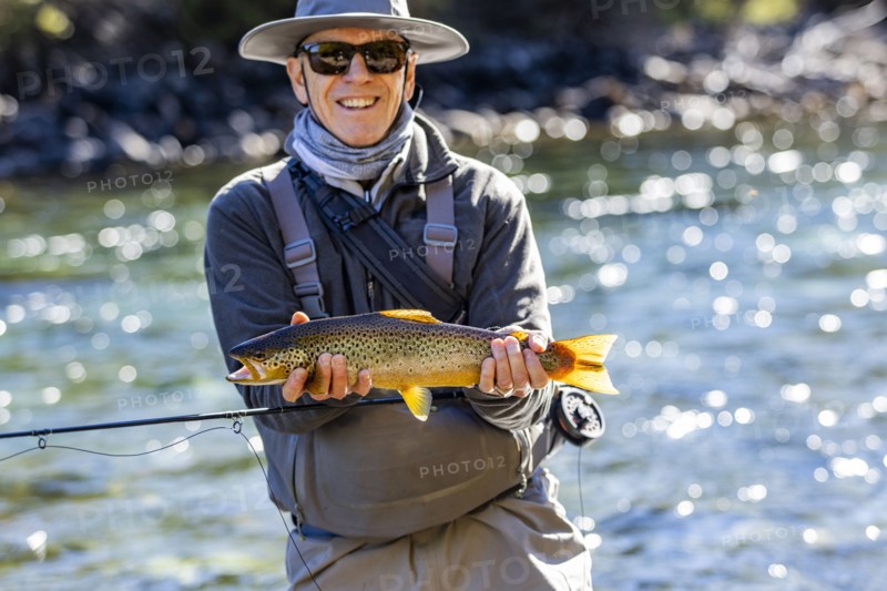 Portrait of smiling fly-fisherman holding native brown trout from Traful River before releasing it unharmed, Estancia Arroyo Verde, Nequen Province, Argentina