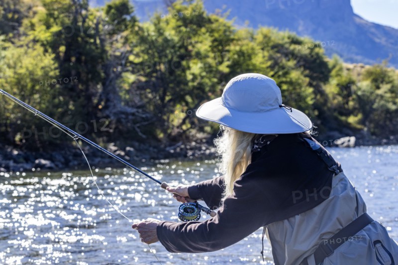 Woman in white hat fly fishing on Traful River on sunny day, Estancia Arroyo Verde, Nequen Province, Argentina