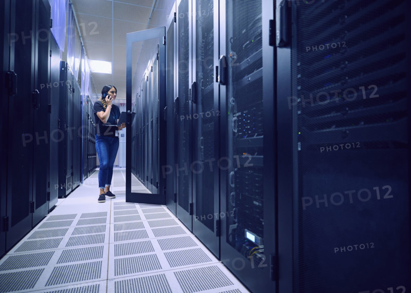 Female technician using laptop and phone in server room 
St, George, Utah, USA