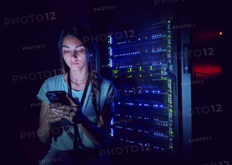Female technician looking at smart phone in server room 
St, George, Utah, USA