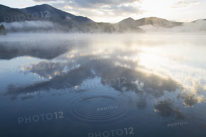 Morning mist over calm Lake Placid surface reflecting clouds and sunlight
Lake Placid, New York USA