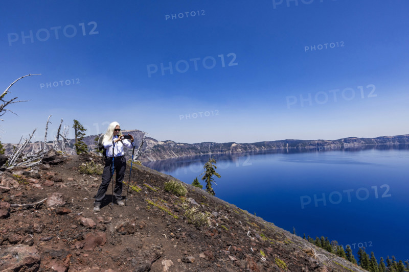 USA, Oregon, Woman with hiking poles taking photos with smart phone by calm Crater lake