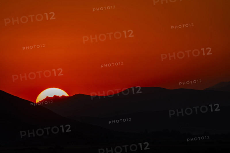 Sun setting behind hills against orange sky