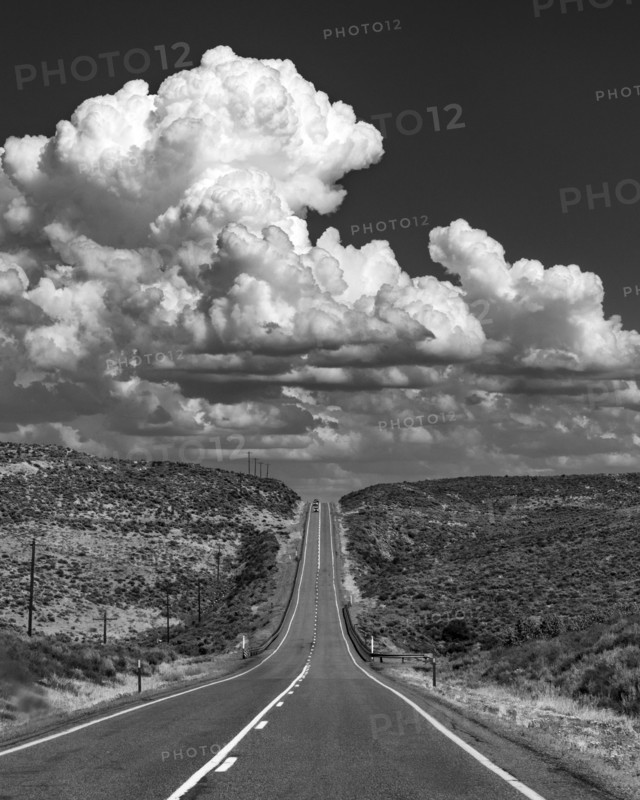 USA, Idaho, Fairfield, Cumulus clouds over empty road crossing landscape, black and white