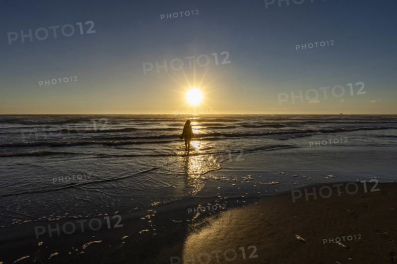 USA, Oregon, Cannon Beach, Woman wading in surf at sunset