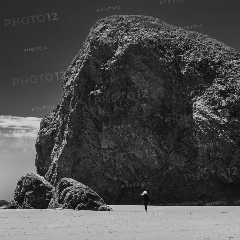 USA, Oregon, Brookings, Rear view of woman walking by huge rocks on Oregon beach, black and white