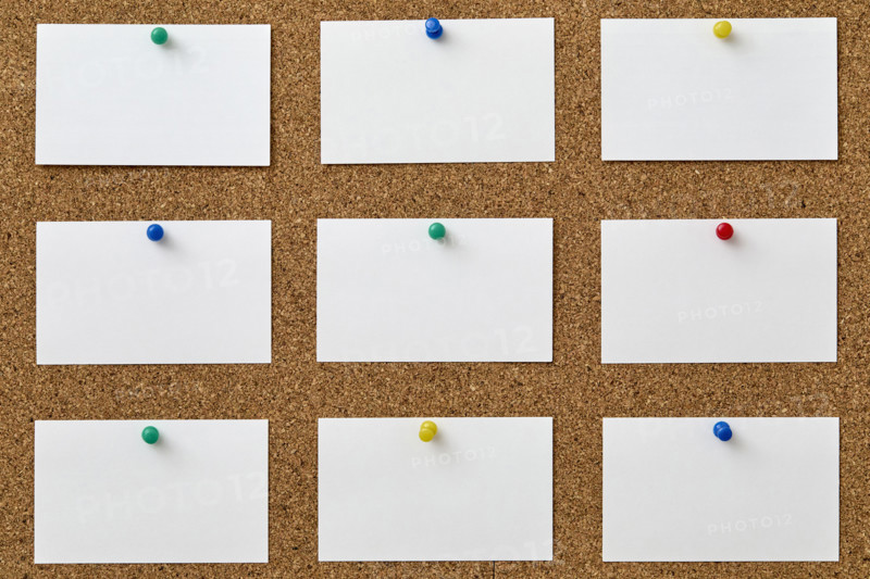 Blank pieces of paper attached to cork board with colorful push pins