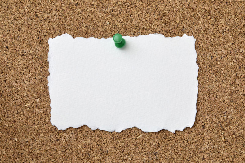 Blank piece of torn paper attached to cork board with push pin