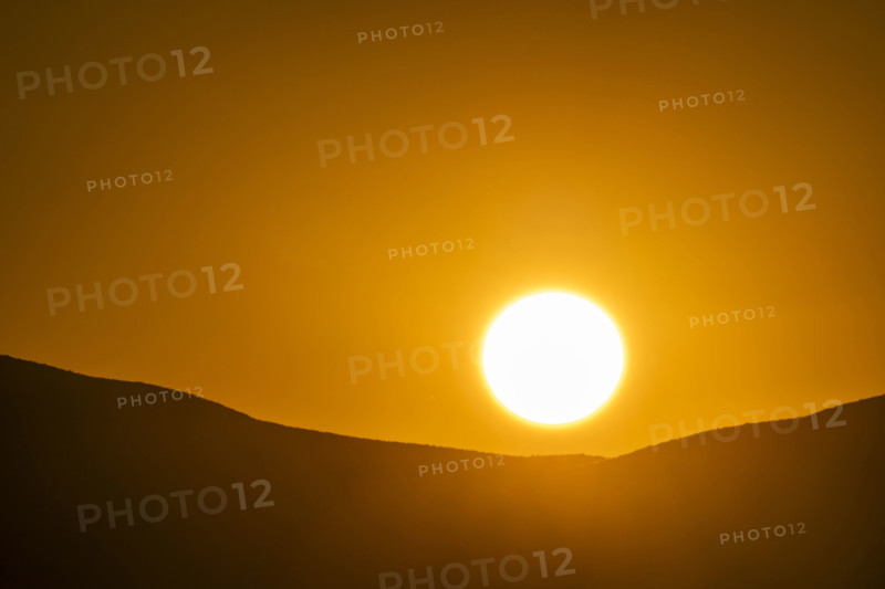 Sun setting over hills against orange sky