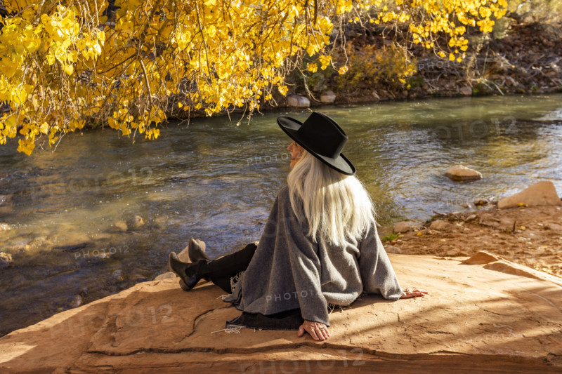USA, Utah, Zion National Park, Rear view of woman in poncho and hat sitting by Virgin River