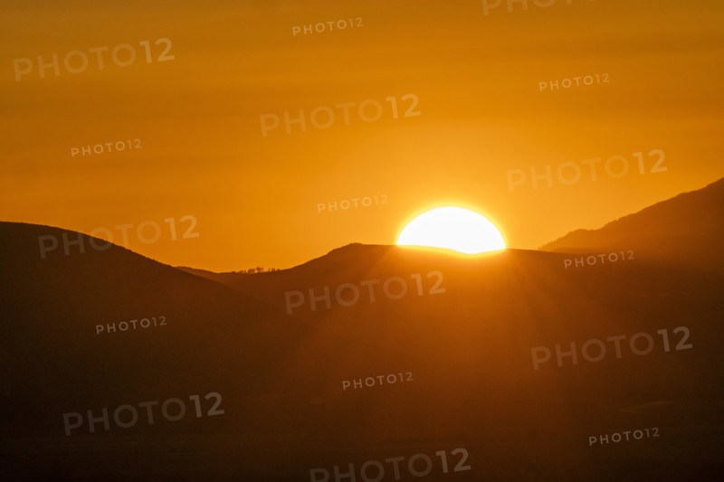 Sun setting above hills against orange sky. Bellevue, Idaho, USA.