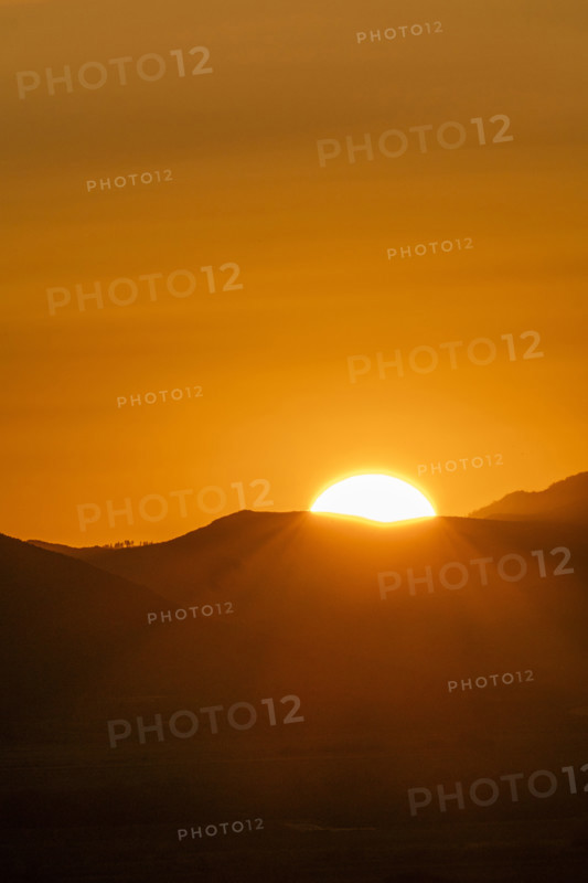 Sun setting above hills against orange sky. Bellevue, Idaho, USA.