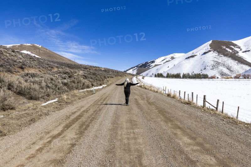 Rear view of woman on empty dirt road in snowy landscape. Bellevue, Idaho, USA.