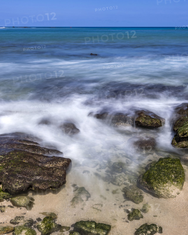Motion blurred ocean waves washing rocks on beach. Kona, Hawaii, USA.