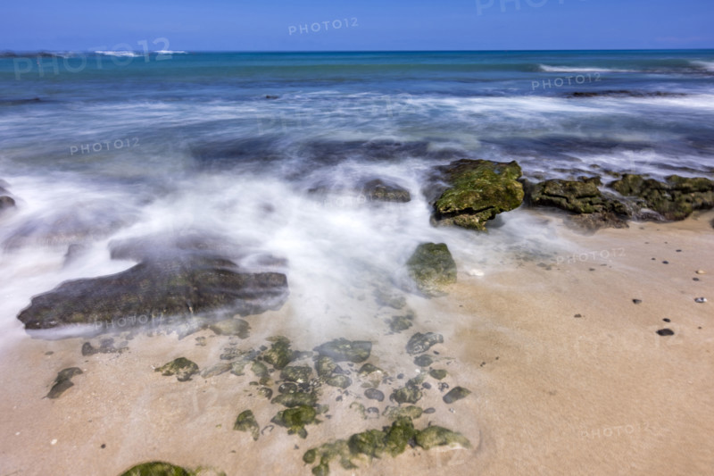 Motion blurred ocean waves washing rocks on beach. Kona, Hawaii, USA.