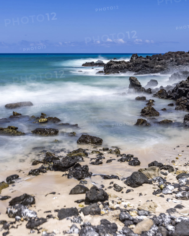 Motion blurred ocean waves washing rocks on beach. Kona, Hawaii, USA.