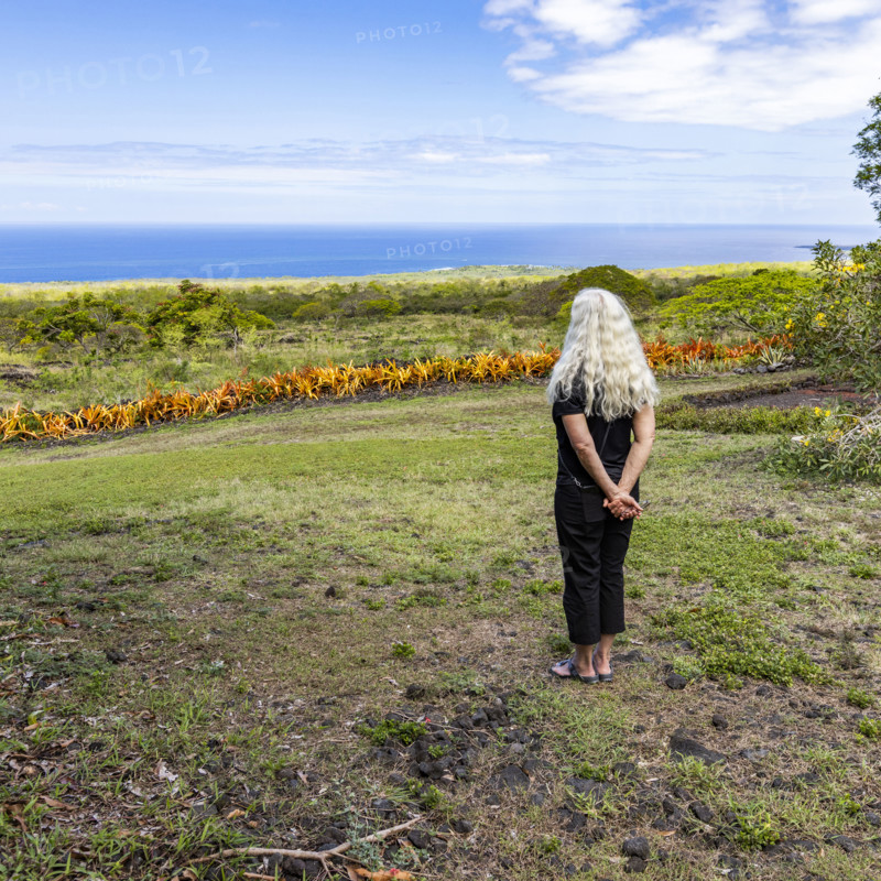 Rear view of woman standing in garden, facing ocean. Kona, Hawaii, USA.