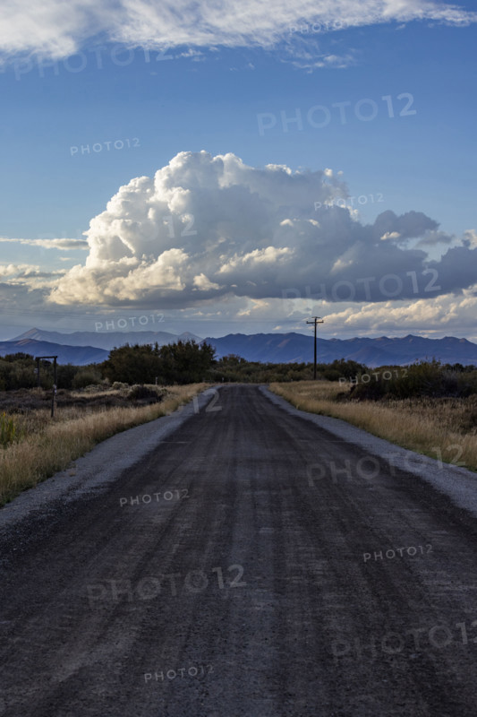 White puffy clouds over empty rural road and mountains. Bellevue, Idaho, USA.