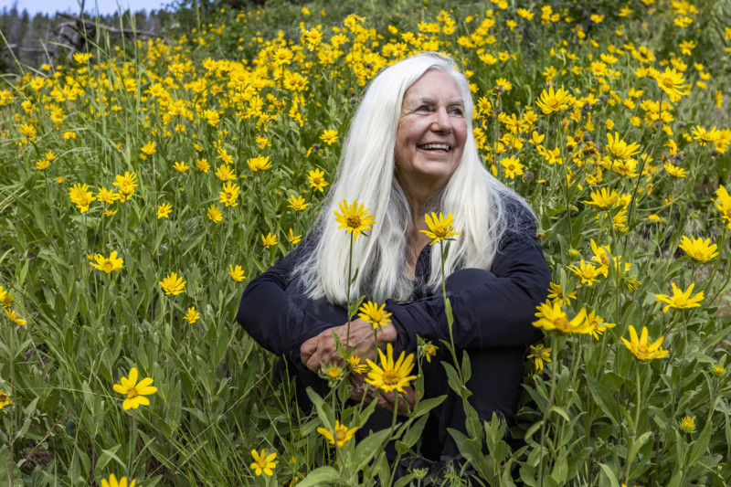 Portrait of senior blonde woman in field of Arrowleaf Balsamroot wildflowers. Sun Valley, Idaho, USA.