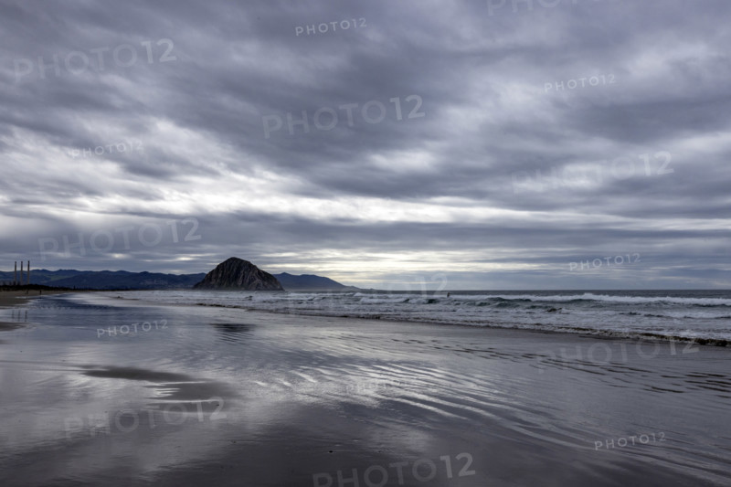 Storm clouds above beach with Morro Rock in distance, Morro Bay, California, USA.