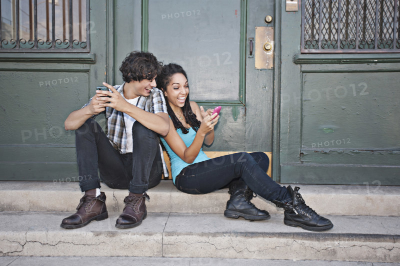Couple using cell phones on front stoop, Los Angeles, California, USA.