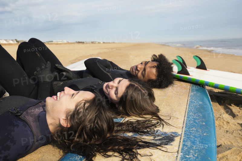 Smiling surfers laying on boards on beach, Virginia Beach, Virginia, USA.