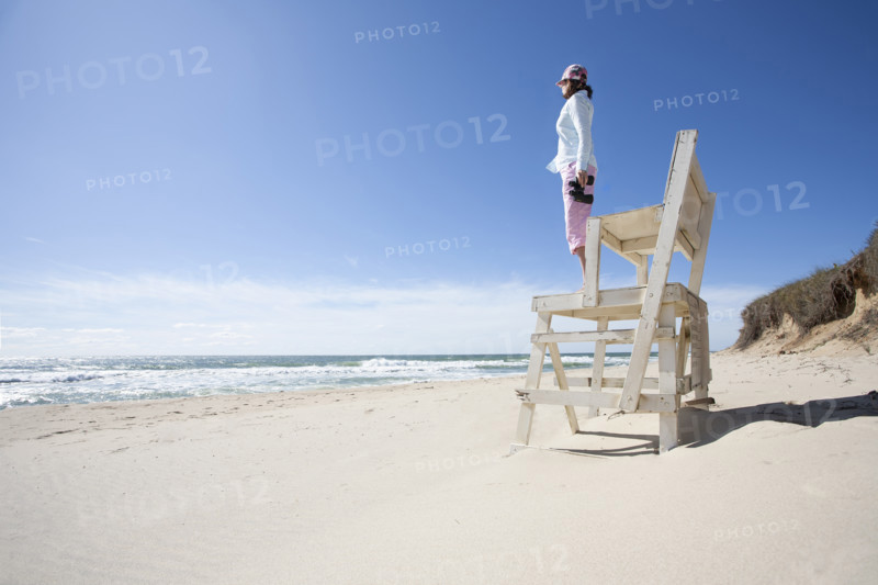 Woman standing on wooden structure on beach and looking out over sea horizon