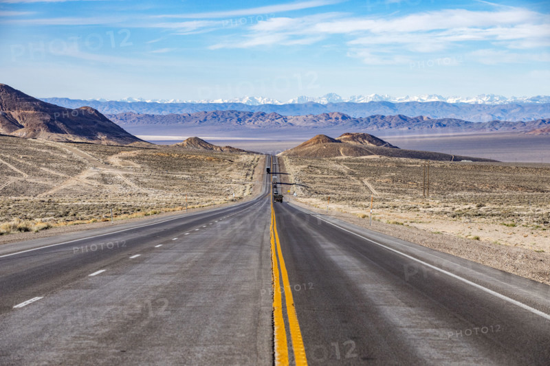 Traffic on desert highway with snowcapped mountains in distance