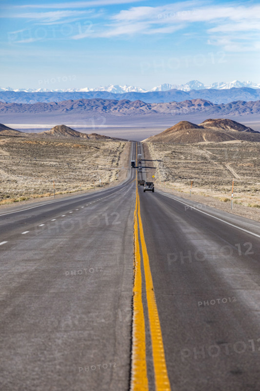 Traffic on desert highway with snowcapped mountains in distance