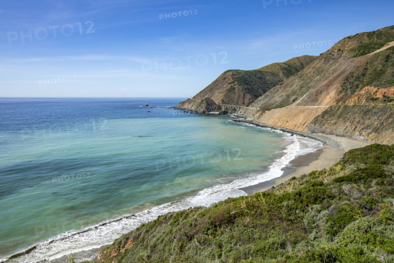 Ocean waves washing Big Sur Coast with Bixby Bridge in distance