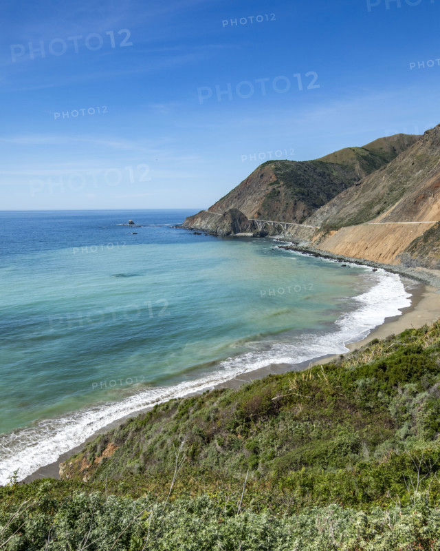Ocean waves washing Big Sur Coast with Bixby Bridge in distance