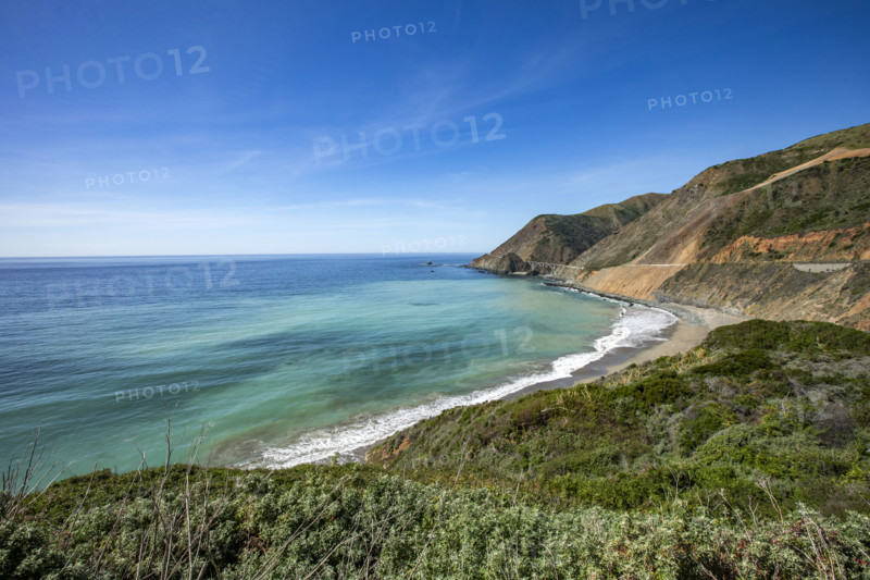 Ocean waves washing Big Sur Coast with Bixby Bridge in distance