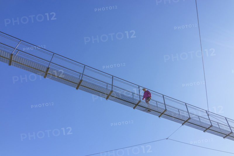 Hiker crossing suspension footbridge against clear sky