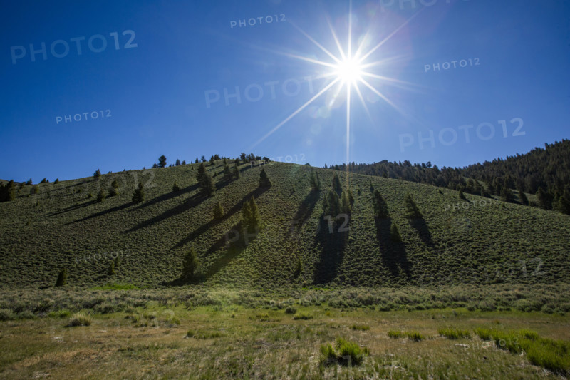 Sun on blue sky above green hill