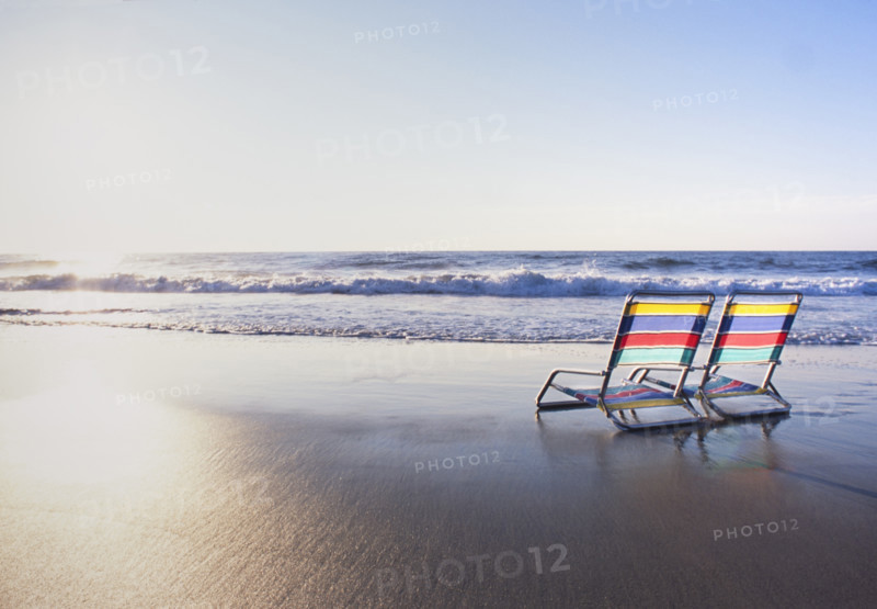 Pair of colorful beach chairs facing ocean at sunrise