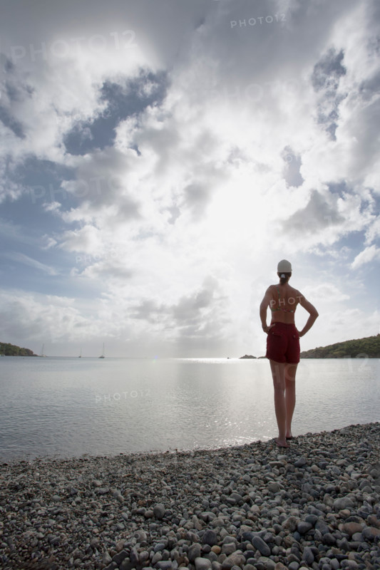 Rear view of woman on pebble beach facing calm sea. St. John, United States Virgin Islands, United States