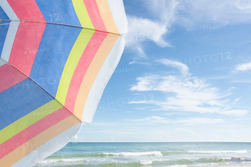 Calm sea with colorful striped beach umbrella in foreground. St. George Island, Florida, United States