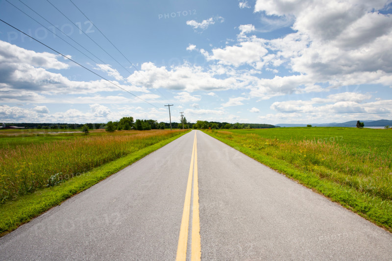 Empty rural road crossing grassy fields. Vergennes, Vermont, United States