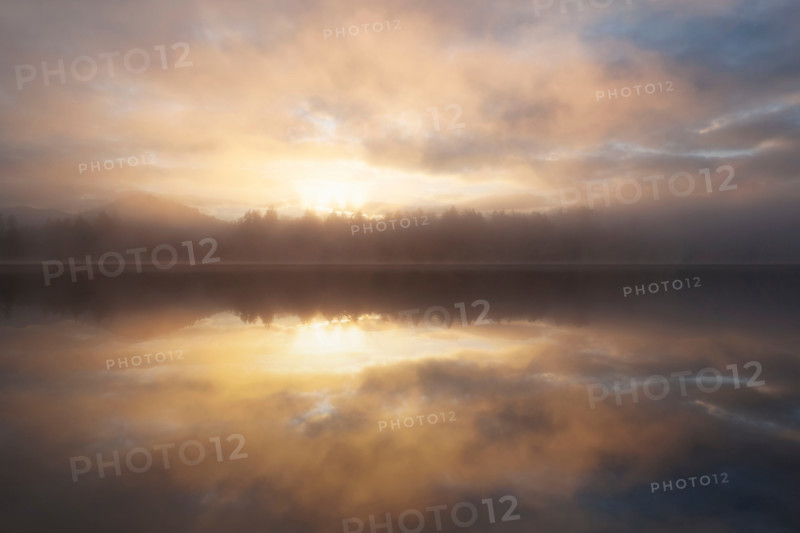 Dramatic sunrise sky reflected in calm lake. Lake Placid, New York State, United States