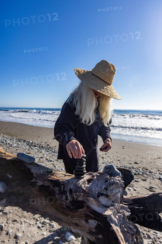 Woman stacking rock cairn on beach. Gold Beach, Oregon, United States