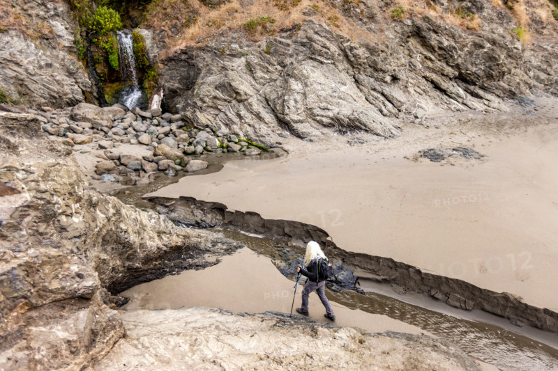 Woman approaching waterfall on Oregon Coast beach. Gold Beach, Oregon, United States