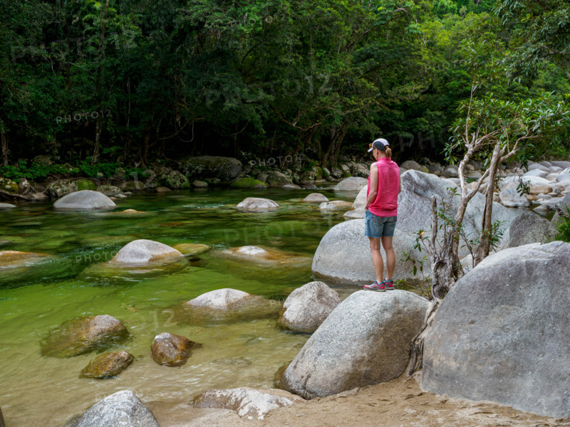 Rear view of tourist standing on boulder in Mossman River. Mossman, Queensland, Australia