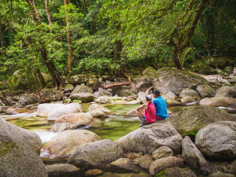 Rear view of couple sitting on boulder in Mossman River. Mossman, Queensland, Australia