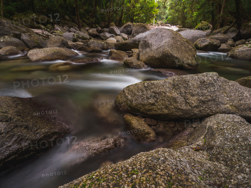 Long exposure of water flowing around rocks in fast moving river. Mossman, Queensland, Australia