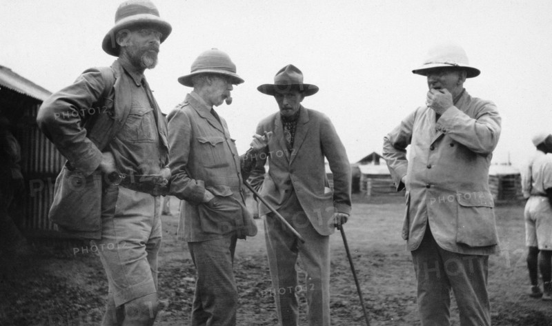 European settlers, Kenya. Exterior shot of four mature European men engrossed in conversation. All of the men wear hats: two carry walking sticks. Kenya, circa 1935. Kenya, Eastern Africa, Africa.