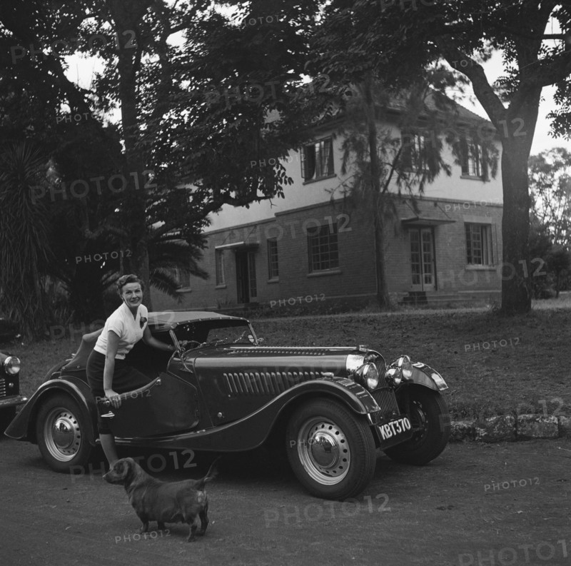 Mrs Douthwaite and car. Mrs Douthwaite and car pictured on the driveway of a large house. There is a small dog in the foreground of the photograph. Kenya, 21 September 1954. Kenya, Eastern Africa, Africa.