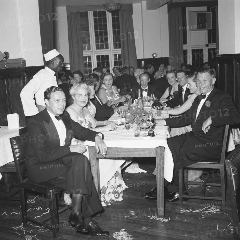 Motor sports dance. Formally dressed guests sit around tables enjoying drinks at a prize presentation evening. The tables are messy and party string litters the floor. Kenya, 26 November 1954. Kenya, Eastern Africa, Africa.